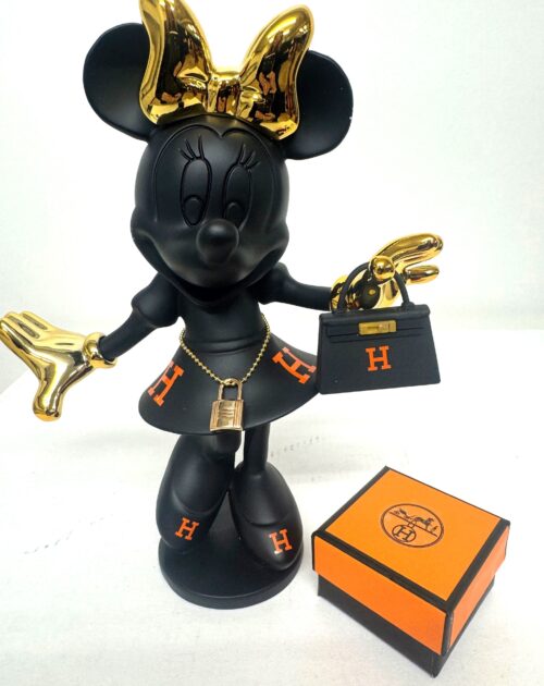 Een matte zwarte sculptuur van Minnie Mouse, versierd met gepolijste gouden en oranje luxe details. Ze staat op een zwarte basis naast een oranje luxe merkdoosje. Ze draagt een gouden strik en gouden handschoenen. Om haar middel draagt ze een gouden heupketting met een gedetailleerd gouden hangslotje. In haar linkerhand houdt ze een kleine, zwarte handtas vast in de stijl van een luxe merk, met een oranje 'H' logo en gouden sluiting. Haar rok en schoenen zijn ook versierd met oranje 'H' monogrammen