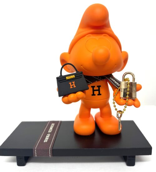 Popart Smurf van 20 cm. hoog in iconisch Hermès oranje voorzien van mini tasje en slotje, gepresenteerd op zwart plateau
