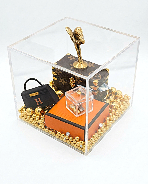 Een handgemaakt miniatuur kunstwerk genaamd Luxury Cube in een heldere acrylglas display 10 cm, met een gouden Spirit of Ecstasy, iconische mini-handtas en gouden kralen.