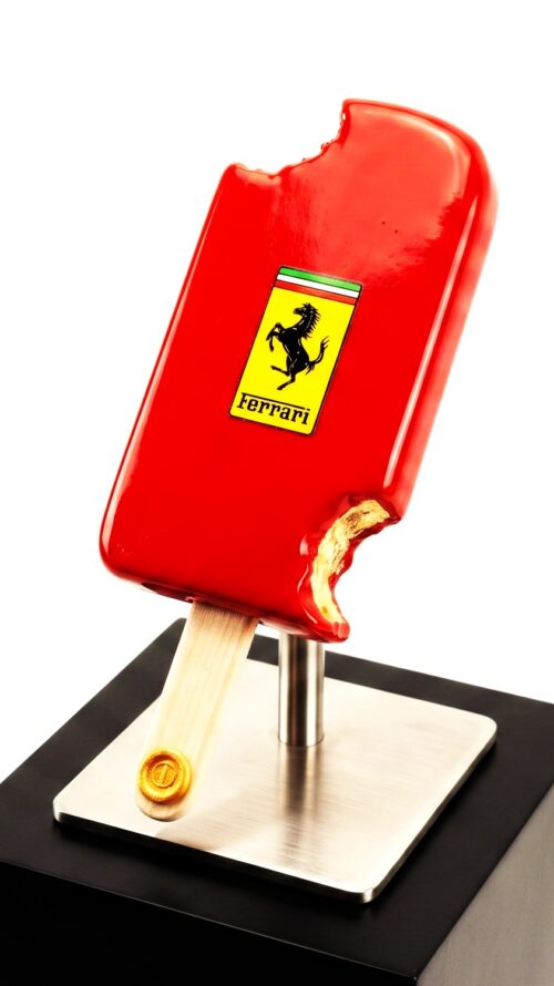 Luxe popart sculptuur van een dieprood Ferrari ijsje met goudkleurige binstenzijde bij de hap, gepresenteerd op een RVS standaard