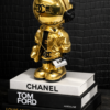 Astro Coco Gold Gouden Chanel‑astronautbeeldje op stapel designboeken met matte zwarte croco‑achtergrond