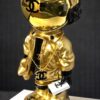 Gouden Chanel‑astronautbeeldje op stapel designboeken met matte zwarte croco‑achtergrond